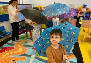 Dzieci chodza po dywanie z kolorowymi parasolkami.