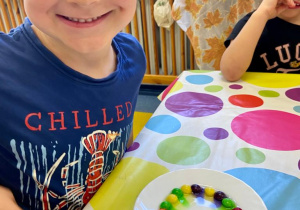 Zajęcia badawcze. Chłopiec obserwuje talerzyk z kolorowymi cukierkami.