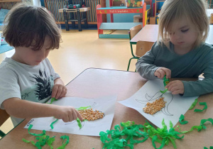 Dzieci tworzą pracę plastyczną z ziarenek kukurydzy.