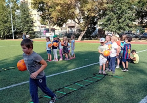 Dzieci wykonują ćwiczenia ruchowe podczas treningu piłkarskiego.