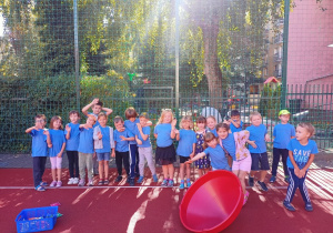 Grupa dzieci stoi na boisku przebrana w stroje sportowe podczas Dnia Przedszkolaka.