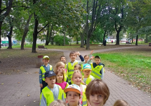 Dzieci w kamizelkach odblaskowych stoją w parku.