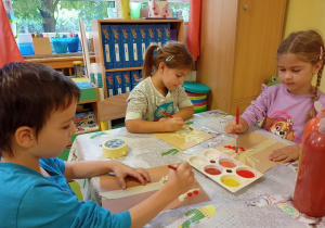 Dzieci malują drzewo farbami plakatowymi.