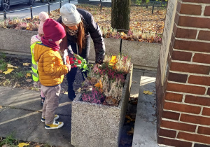 Dziewczynka z grupy 1 i chłopiec z grupy 2 składają kwiaty przy pomniku.