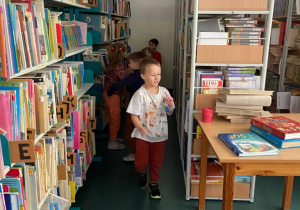 Biblioteka szkolna. Dzieci szukają w bibliotece wśród półek z książkami ukrytych pluszowych misiów.