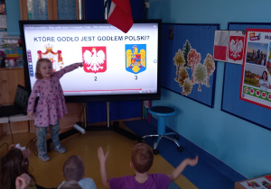 Dziewczynka wskazuje godło Polski na dużym ekaranie.