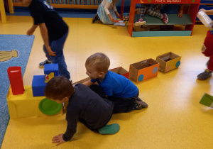 Dzieci bawią się na podłodze pociągiem zrobionym z pudełek.