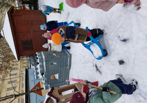Dzieci odśnieżają i wożą śnieg na taczkach.