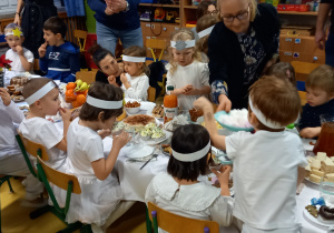Dzieci siedzą przy wigilijnym stole i jedzą.