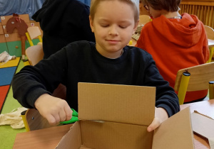 Chłopiec tworzy zabawkę z kartonu.