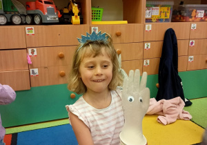 Dziewczynka pokazuje skonstruowaną z papierowego kubka i gumowej rękawiczki zabawkę służącą regulowaniu napięcia i łagodzenia stresu.