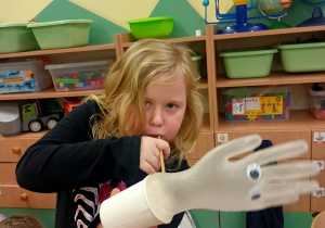 Dziewczynka dmucha w zabawkę wykonaną z papierowego kubka i gumowej rękawiczki.