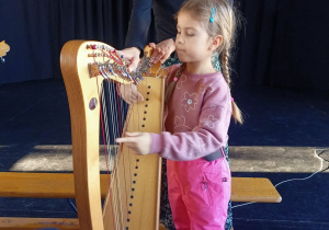 Dziewczynka próbuje grać na harfie.