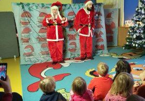 Przedstawienie świąteczne. Dzieci siedzą na dywanie i patrzą na dwóch świętych Mikołajów.