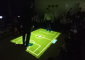 Dzień Babci i Dziadka. Dziadkowie grają w piłkę nożną na zielonym multimedialnym dywanie.