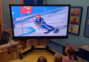 Dzieci oglądają pokaz sportów zimowych na tablicy multimedialnej - slalom narciarski.
