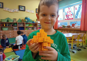 Chłopiec pokazuje budowlę skonstruowaną z klocków.