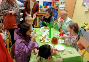 Dzieci oraz ich dziadkowie częstują się ciastem i herbatą podczas Dnia Babci i Dziadka w przedszkolu.