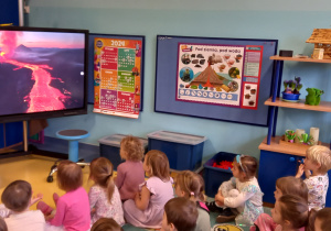 Dzieci oglądają wybuch wulkanu i płynącą lawę na dużym ekranie.