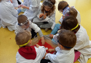 Dzieci ubrane w białe fartuchy szukają w pudełkach modelu krwi podanych składników.