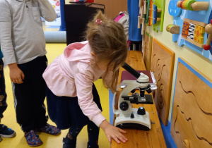 Dziewczynka patrzy w okular mikroskopu.