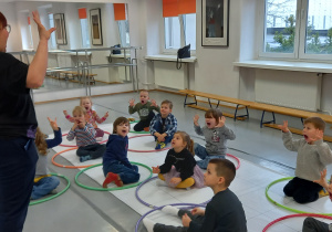 Zajęcia w Domu Kultury. Dzieci siedzą na podłodze w kołach hula-hop i ćwiczą aparat mowy.
