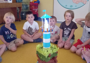 Dzieci siedzą wokół modelu latarni morskiej ze światełkiem.