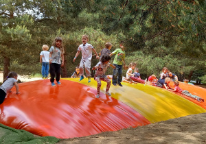 Dzieci skaczą na dmuchanej kolorowej trampolinie plażowej.