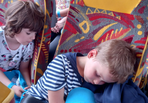 Dziewczynka i chłopiec w niebieskich czapkach z daszkiem śpią na fotelach w autokarze.