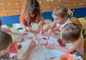 Dzieci malują czerwoną farbą sylwetkę raczka narysowaną na białym materiale.