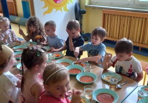 Dzieci jedzą zupę pomidorową przy wspólnym dużym stole.