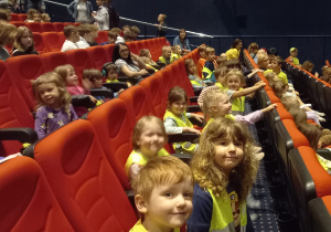Dzieci siedzą na widowni teatru w czerwonych fotelach.