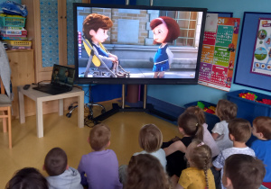 Dzieci oglądają film na dużym ekranie o dziewczynce i niepełnosprawnym chłopcu.