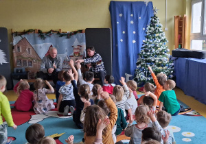 Koncert. Dzieci siedzą przed muzykami i podnoszą ręce do góry.