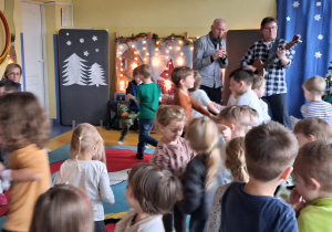 Koncert. Muzycy grają na gitarze i fujarce, a dzieci tańczą.