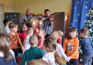 Koncert. Muzycy grają na gitarze i bębenku, a dzieci tańczą.