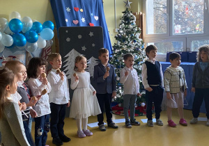 Dzień Babci i Dziadka. Dzieci stoją w półkolu, grają na grzechotkach i śpiewają piosenkę.