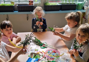 Dziewczynki siedzą przy stoliku i zaplatają palemki wielkanocne.