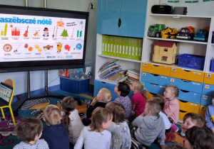 Dzieci siedzą na dywanie i słuchają wiersza po kaszubsku.