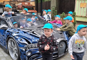 Wycieczka. Dzieci stoją wokół niebieskiego sportowego samochodu.