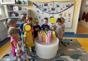 Dzieci stoją na dywanie a przed nimi widać stolik, na którym stoją torebki z prezentami.