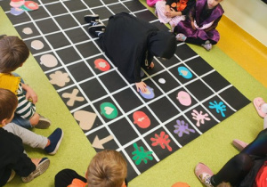 Dzieci siedzą wokół maty do kodowania i przekładają obrazki dyń.