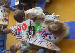 Dzieci naklejają listki na szablon drzewa.