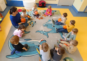 Dzieci siedzą w kole z dynią w ręku.