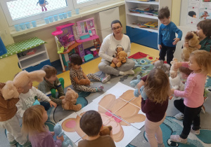 Dzieci siedzą na dywanie wokół ułożonych puzzli i przytulają swoje misie.