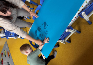 Chłopiec z pomocą pani odciska swoją rękę na kartce.