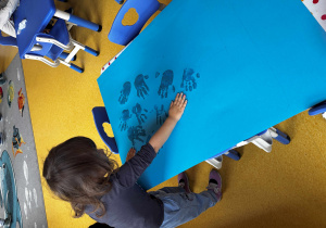 Dziewczynka odciska swoją dłoń na kartce.