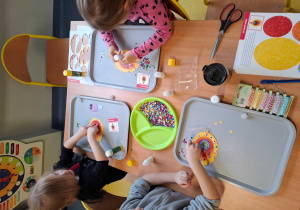 Zajęcia plastyczne, dzieci wykonują ozdobę na choinkę z papieru.