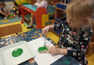 Dziewczynka maluje widelcem choinkę.
