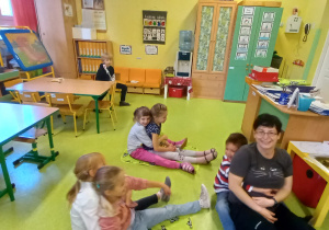 Dzieci siedzą w parach na podłodze razem z nauczycielką.
